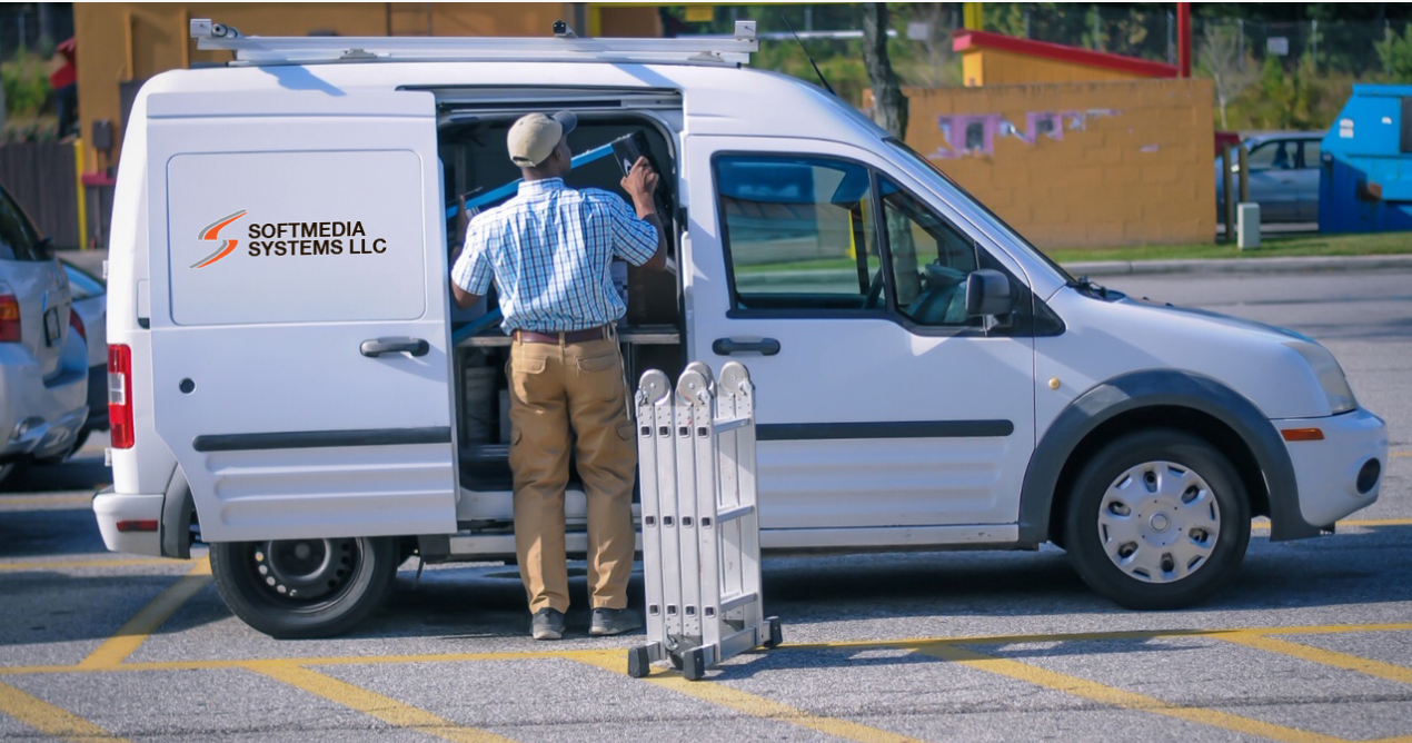Soft Media Systems technician preparing equipment beside the company service van.